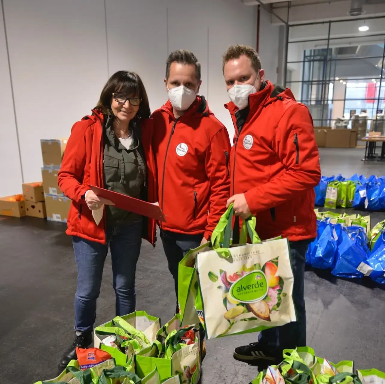 Drei Menschen aus dem Festmahl-Team in roten Jacken mit gepackten Festmahl-Tüten